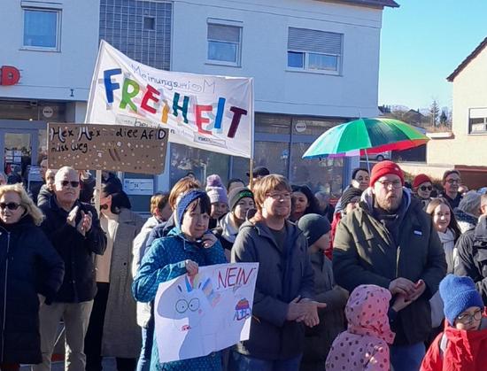 Demo-Teilnehmende Banner mit der bunten Aufschrift Freiheit, ein Regenbogenregenschirm und anderen handgemalte Plakaten.